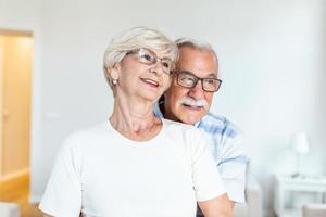 pareja mayor de pie en la sala de estar. pareja de ancianos sintiéndose feliz, mirando a lo lejos. marido alegre abrazando a su esposa. concepto de amor de ancianos foto