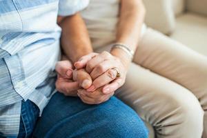 Close up of mature old husband and wife hold hands show love and care. Senior couple holding hands while sitting together at home. Elderly relationships, marriage concept photo