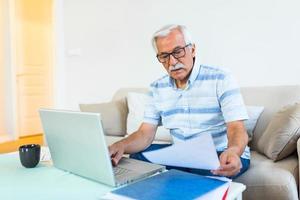 Mature businessman sit on sofa working on computer wireless device using e-banking application paying bills online, typing e-mail solve issues distantly, older generation and modern tech usage concept photo