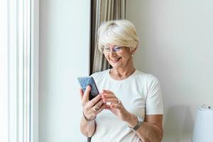 senior woman using smartphone  gray hair woman relaxing at home reading her text messages on her mobile phone with a quiet smile. Senior female texting or playing an online game on smartphone at home. photo
