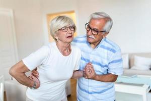 Senior couple at home. Handsome old woman is having back pain and her attractive old husband supports her. photo