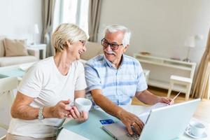 Senior couple smiling checking utility bills or insurance at computer with easy access, elderly users of technology photo