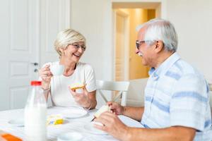 Happy senior couple having breakfast at home. Elderly couple smiling to each other. Old couple having fun during breakfast. Food, eating, people and healthy food concept photo