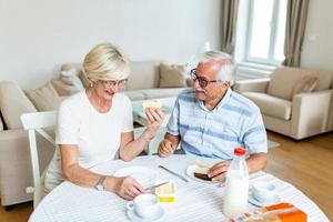 Happy senior couple having breakfast at home. Elderly couple smiling to each other. Old couple having fun during breakfast. Food, eating, people and healthy food concept photo