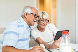 Senior couple smiling and looking at the same tablet hugged. Indoor, at home concept. Mature and retired man and woman using technology - lockdown and quarantine lifestyle photo