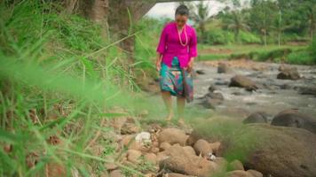 asiatique femme en marchant sur le bord de le rivière tandis que portant une rose robe et vert jupe dans maquillage avec une lot de Roche video