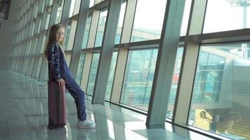 adorable niña en el aeropuerto cerca de una gran ventana jugando con su teléfono video