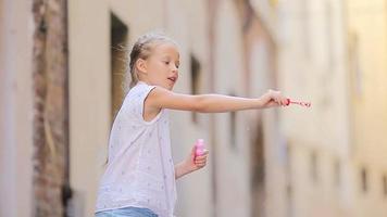 Little girl blowing soap bubbles in narrow street in european city. Portrait of caucasian kid enjoy summer vacation in Rome video
