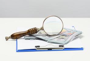 a stack of one hundred dollar bills and a wooden magnifier on a white background. Budget analysis, income and expenses, problem finding photo