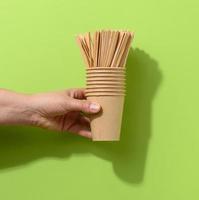 hand hold brown paper cardboard cups and wooden stirring sticks on a green background photo