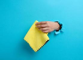 female hand sticking out of a torn hole in a blue paper background and holding a dry rag photo