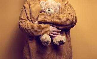 woman in orange knitted sweater hugs cute brown teddy bear. The concept of loneliness and sadness, depression photo