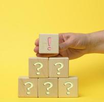 hand hold wooden cube with exclamation marks and a question mark  on a yellow background photo