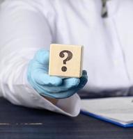 wooden cube with a question mark in the doctor's hand on a blue background. The concept of finding an answer to questions photo