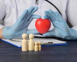 wooden figurines of a family and a red heart in the hands of a doctor. Family health insurance concept photo