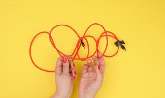 female hand holds twisted cable for charging mobile devices in a red textile wrapper on a yellow background photo