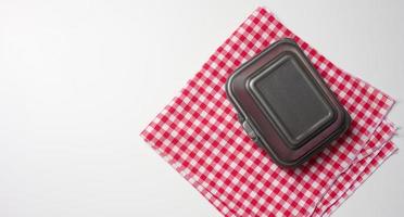 closed gray disposable container and a red napkin on a white table, top view photo