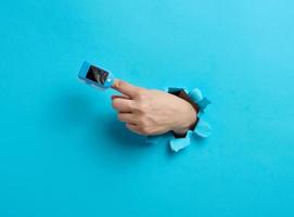 an oximeter for measuring oxygen in the blood is worn on the index finger, part of the hand is sticking out of a torn hole in the blue paper photo