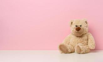 marrón osito de peluche oso con un triste cara se sienta en un blanco mesa, rosado antecedentes foto