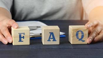 man sits at a table and holds cubes. inscription  frequently asked questions on wooden blocks on a blue background photo