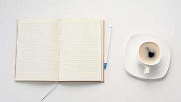 abierto cuaderno con blanco blanco hojas y un taza de café en un blanco mesa, lugar de trabajo, parte superior ver foto