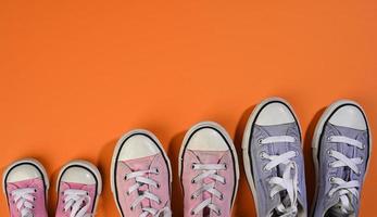 many multi-colored well-worn textile sneakers of different sizes on a orange background, top view photo