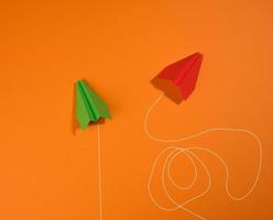 two paper airplanes with different trajectory of movement on an orange background photo