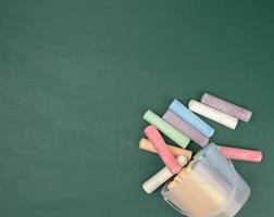 crayones multicolores en el fondo de la pizarra de la escuela de tiza verde foto