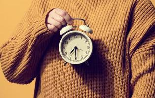 round alarm clock in a woman's hand, the time is half past seven in the morning. Woman in orange sweater photo