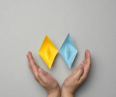 Two yellow-blue paper boats in female palms on a gray background photo