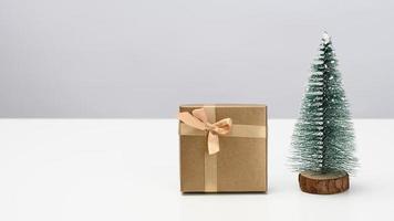 caja es envuelto en marrón papel y un decorativo Navidad árbol en un blanco mesa. festivo antecedentes foto
