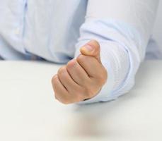 female hand folded into a fist on a white table. Strict leader, aggression and pressure on the person photo