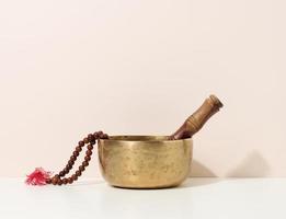 copper singing bowl and wooden clapper on a white table. Musical instrument for meditation, relaxation, various medical practices related to biorhythms, normalization of mental health photo