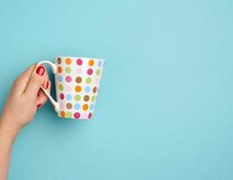 female hand holds a ceramic mug on a blue background, break time and drink coffee photo