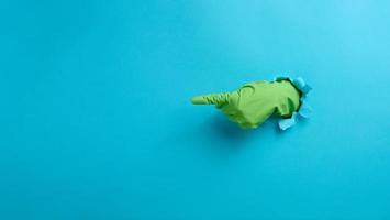 a hand in a green latex glove points a finger on a blue background. Place for inscription of discounts, offer or announcement. photo