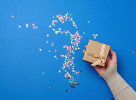 female hand in a golden sweater hold closed square blue box with a bow photo