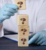 wooden cube with a question mark in the doctor's hand on a blue background. The concept of finding an answer to questions photo
