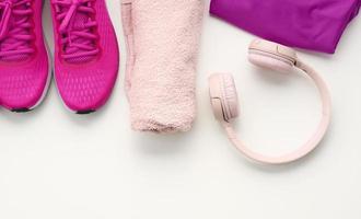 pair of textile purple sports sneakers, wireless headphones, a towel and a bottle of water on a white background. Sportswear photo
