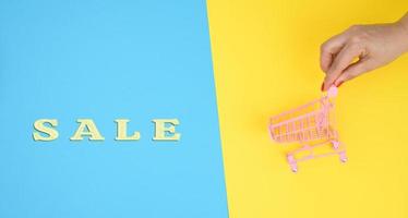 female hands hold an empty metal miniature trolley on a blue background. Sale concept photo