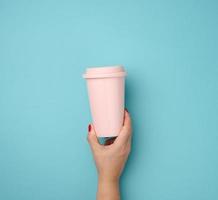 female hand holding a pink ceramic mug with a plastic lid on a blue background photo