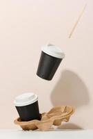 two brown cardboard cups with a white plastic lid. Disposable tableware levitates against a beige background photo