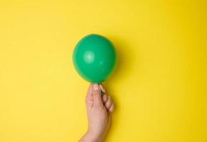 female hand holding an inflated green air balloon on a yellow background photo