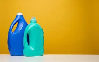 plastificado azul grande botellas con líquido detergente estar en un blanco mesa, amarillo antecedentes foto