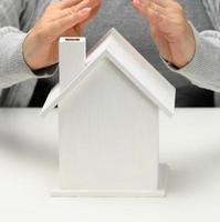 female hands folded to each other over a wooden miniature model house on a white background. Real estate insurance concept, environmental protection, family happiness photo