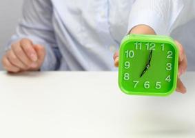 woman's hand holds a green square alarm clock, the clock shows seven in the morning. Wake up early, start the day photo