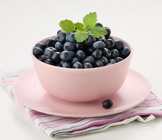 Ripe blueberry in a pink ceramic plate on a white table, tasty and useful berry photo