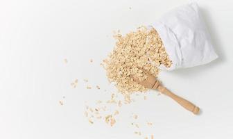 raw oatmeal in a white paper bag and a wooden spoon on a white table, breakfast porridge photo