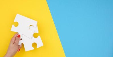 female hand holds a fragment of a white large puzzle on a blue background, the concept of finding an idea photo