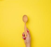 female hand holding empty wooden spoon on yellow background photo