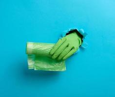hand holds a bundle of transparent garbage bags on a blue background. A part of the body sticks out of a torn hole in the paper photo